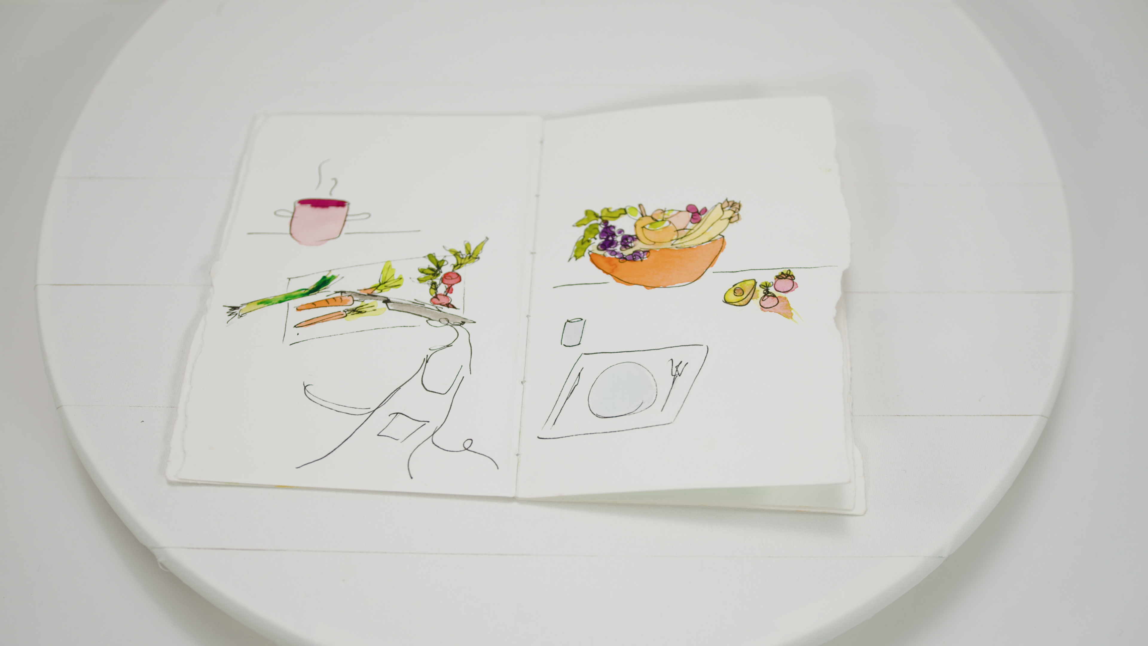 An open water colour book with a cutting board vegetables and an apron on the left page and a bowl of fruits with plate and set cutlery on the right page.