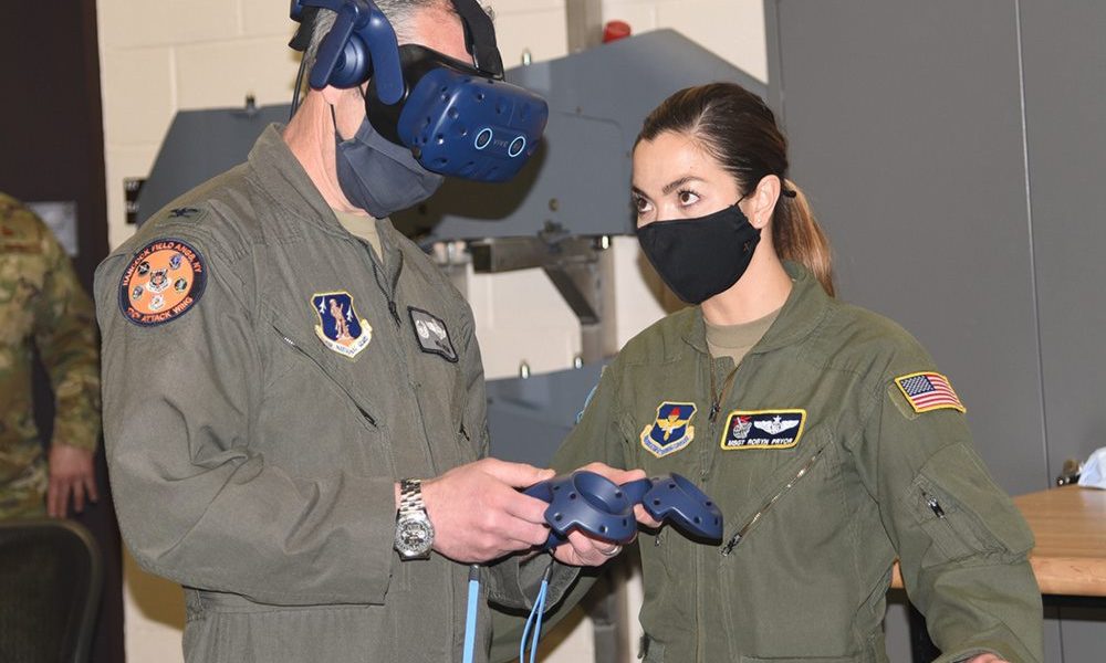 Two airmen in masks, one using a VR headset.