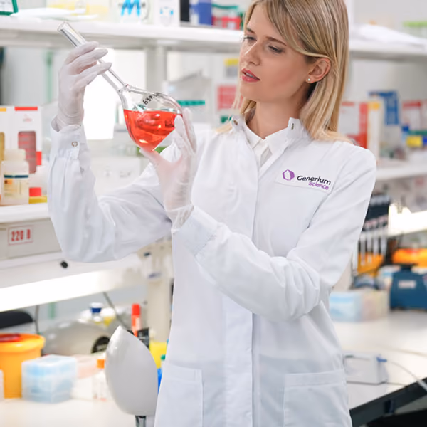 Female scientist in a lab coat examining a glass flask with red liquid in a laboratory.