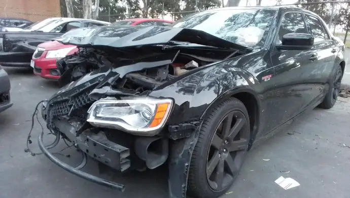 Severely damaged black Chrysler sedan written off after a car accident, showing extensive front-end structural damage typical of statutory write-off vehicles in Australia.