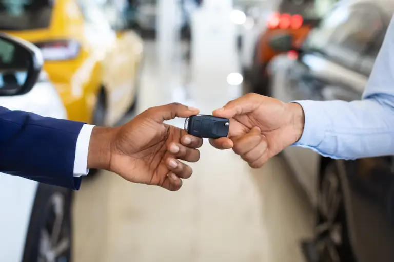 Black Male Customer Taking Car Keys From Seller In Dealership Center, Unrecognizable African American Man Purchasing Or Renting New Vehicle In Auto Showroom, Cropped Image, Selective Focus