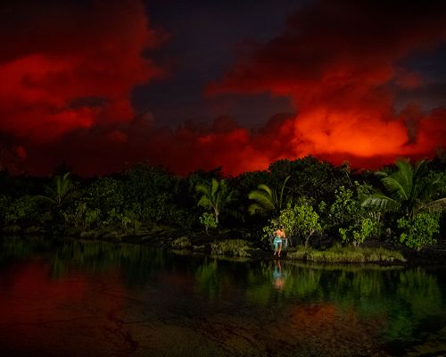 Clouds glowing red from lava as a Hawaiian fisherman prepares to throw net in Kapoho, Puna, Hawaiʻi during the eruption of 2018