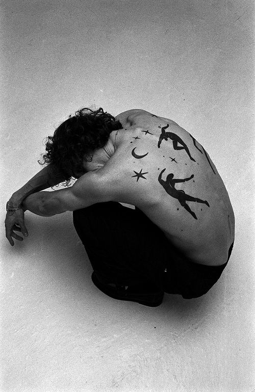 Roberto Ecclesia Jr. is crouching on the floor. Visible are the back of his head and the tattoos on his back.