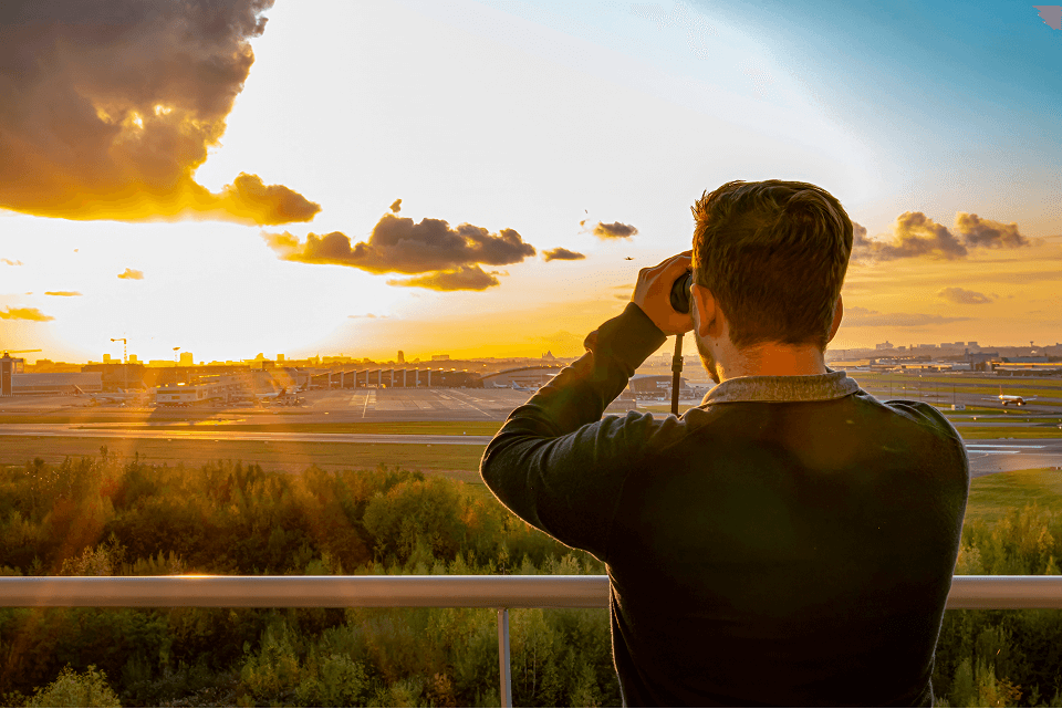 Person looking at the airport from a distance, with an warm, golden sunset in the background.
