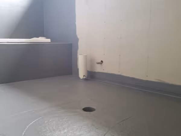 Bilde av et tomt rom med et dreneringshull i gulvet og rørutløp på veggen, klart for installasjon av baderomsinnredning.