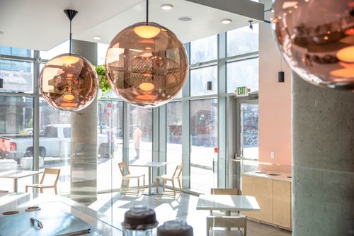 Copper globe pendant lights in a modern café interior with large floor-to-ceiling windows, light wooden furniture, and a spacious layout.