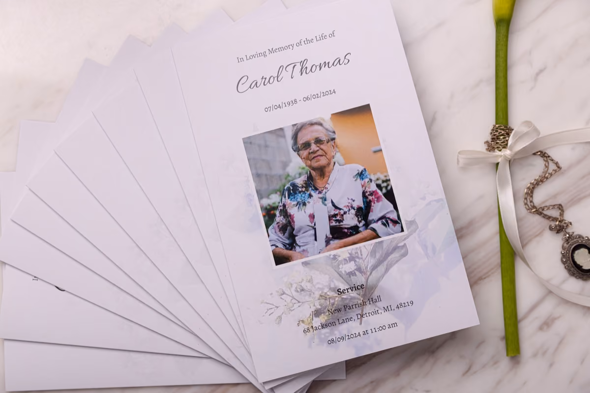 A stack of folded funeral programs, the top one showing a name, dates and portrait