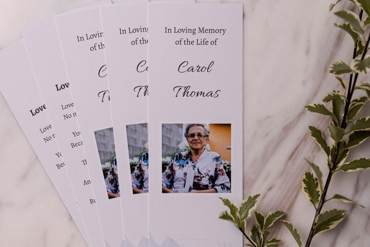 A fan of remembrance bookmarks on marble, each carrying a name, dates and a portrait photograph