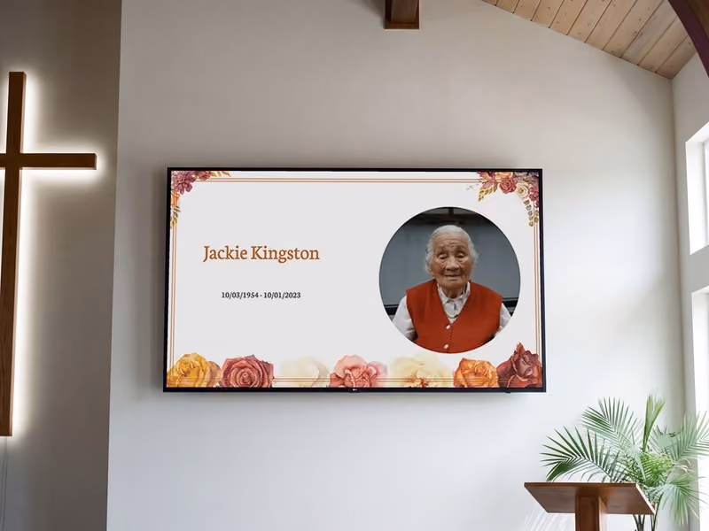 A memorial welcome screen with an autumn floral design, shown on a screen in a chapel
