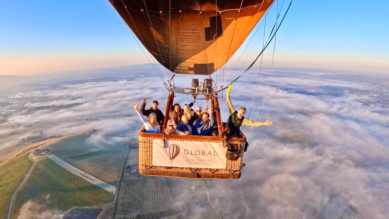 Guests cheer mid-flight in a Global Ballooning Australia hot air balloon basket, soaring above a sea of fog over the Yarra Valley at sunrise