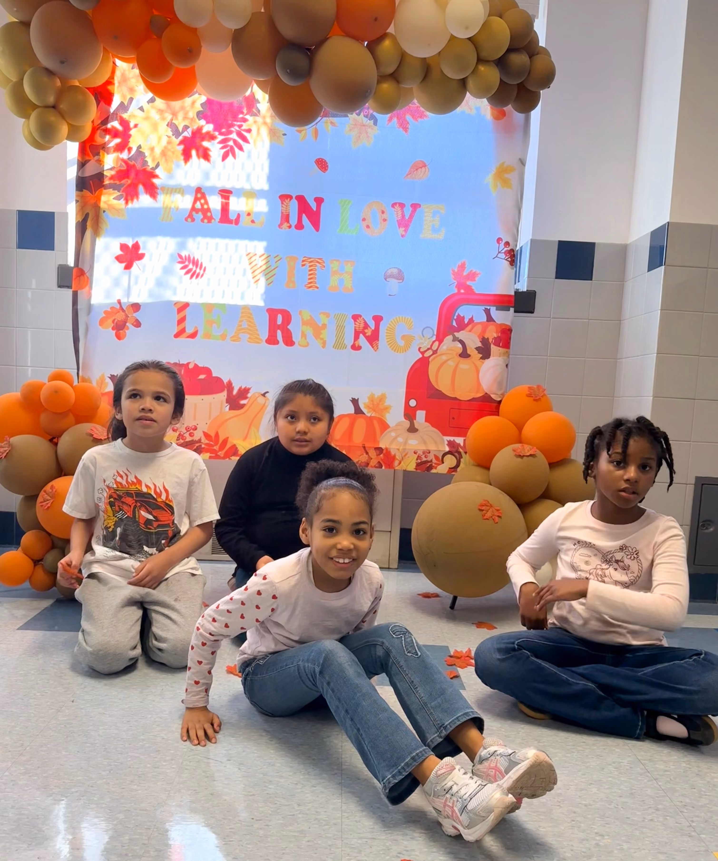 Four students posing at a fall-themed school learning display