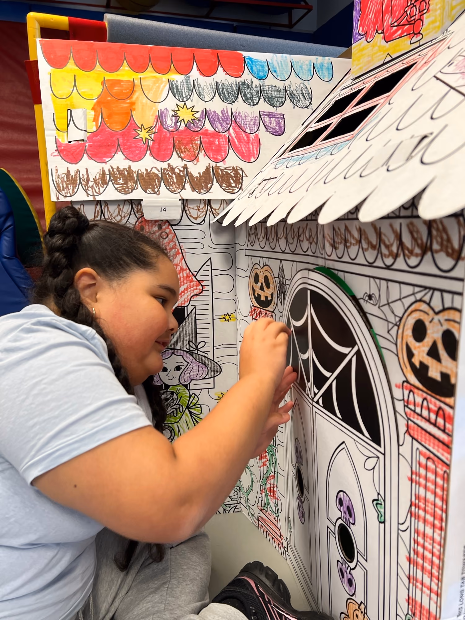 Student coloring a large Halloween-themed cardboard playhouse