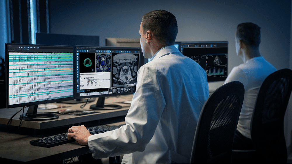 Radiologist analyzing multiple CT scan images on dual monitors in a medical imaging lab.