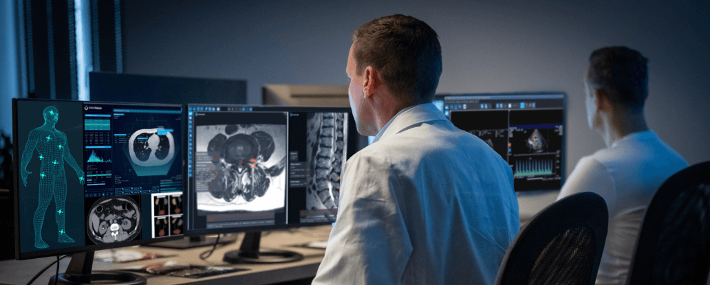 Dois radiologistas estão vendo imagens médicas em vários monitores de computador, concentrados em exames cerebrais numa sala meio escura.