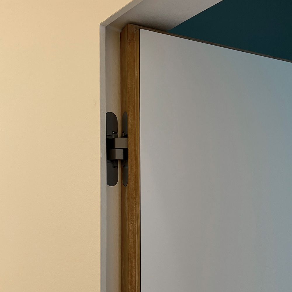 Nærbillede af skjult dørhængsel i dørkarmen på en hvid dør.