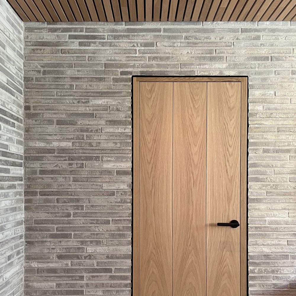 Trædør med sort greb i grå murstensvæg under loft med trælister.