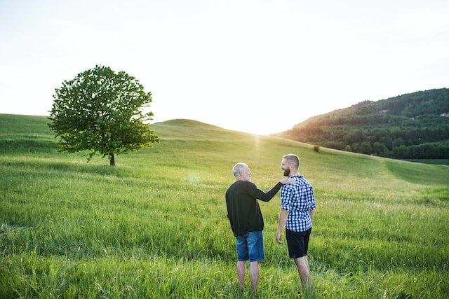 Father and adult son talking together in a sunlit green field
