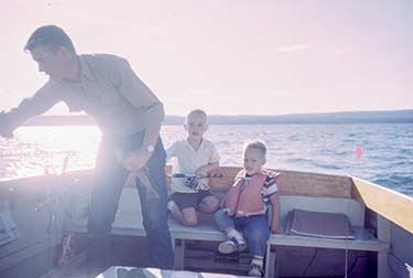 Father steering a small boat with two young children aboard