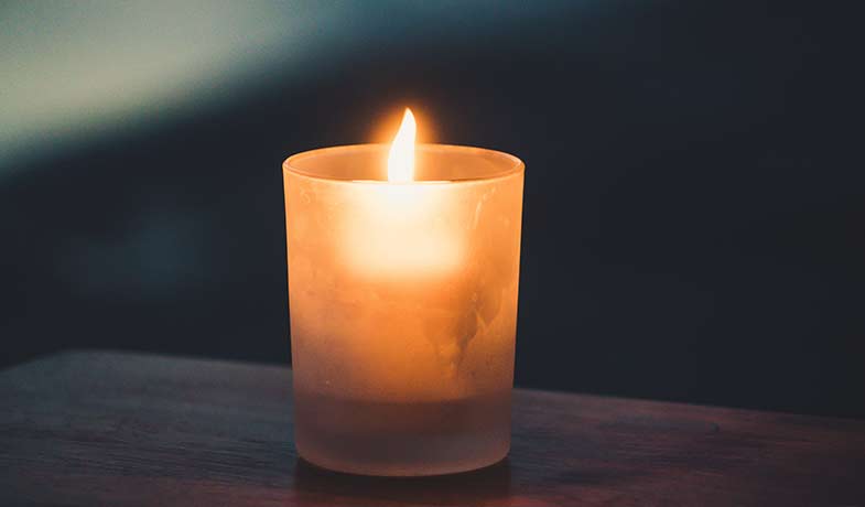 Lit candle glowing in a frosted glass holder at night