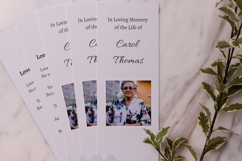 Printed memorial bookmarks featuring a portrait and name, fanned across a marble surface.