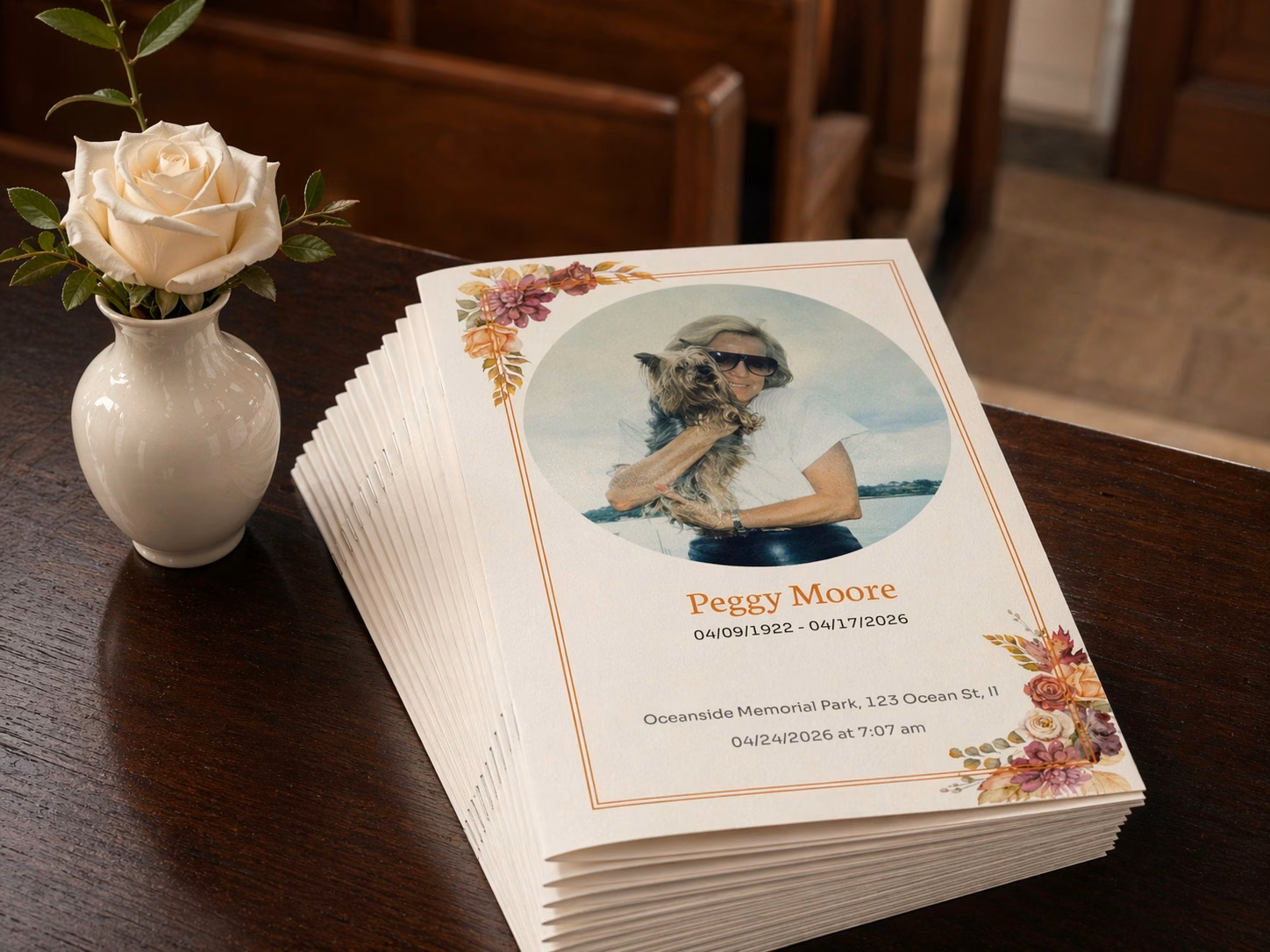 Peggy Moore funeral programs stacked on a wooden table beside a white rose.