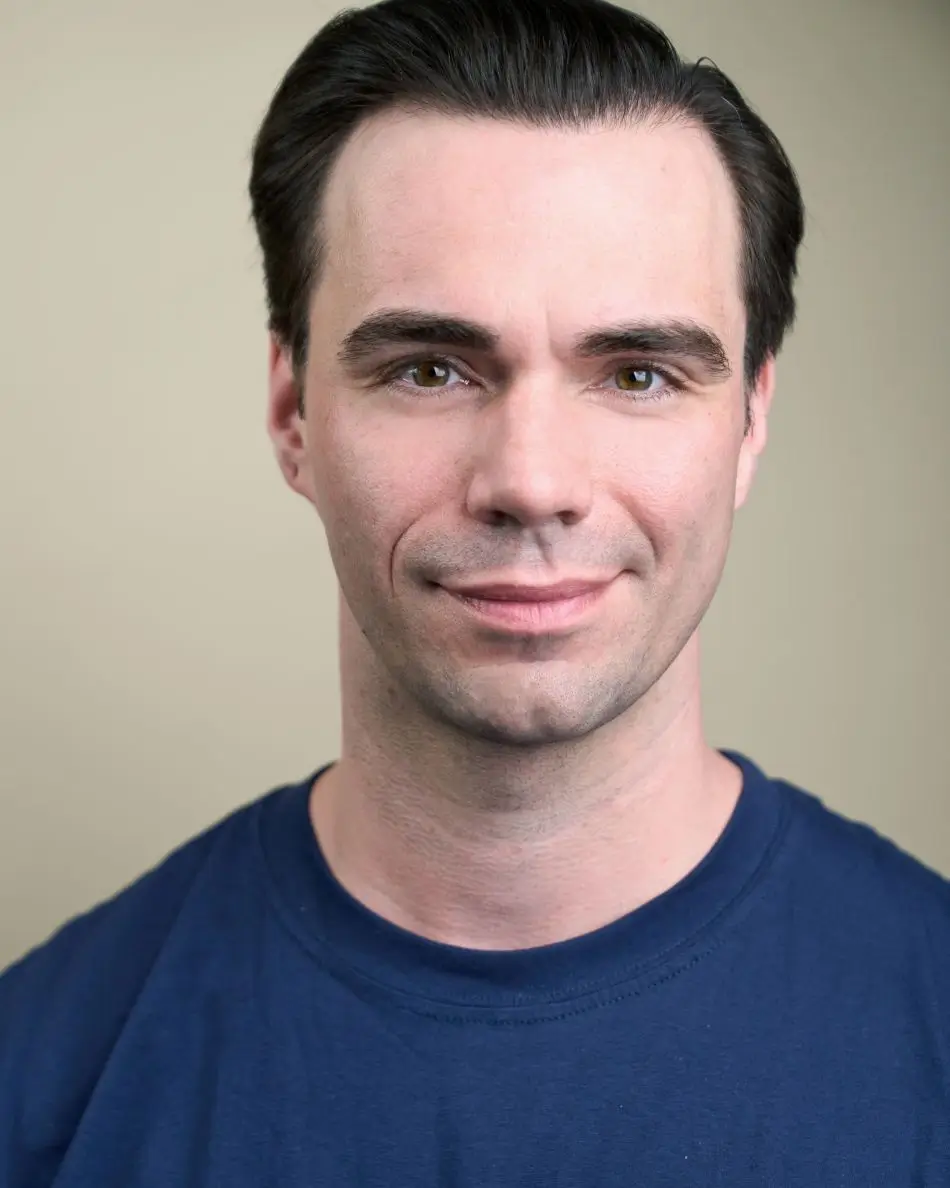 Atlanta men’s actor headshot — male actor with dark hair, subtle confident smile in navy shirt against neutral background, classic theatrical stage-ready look.