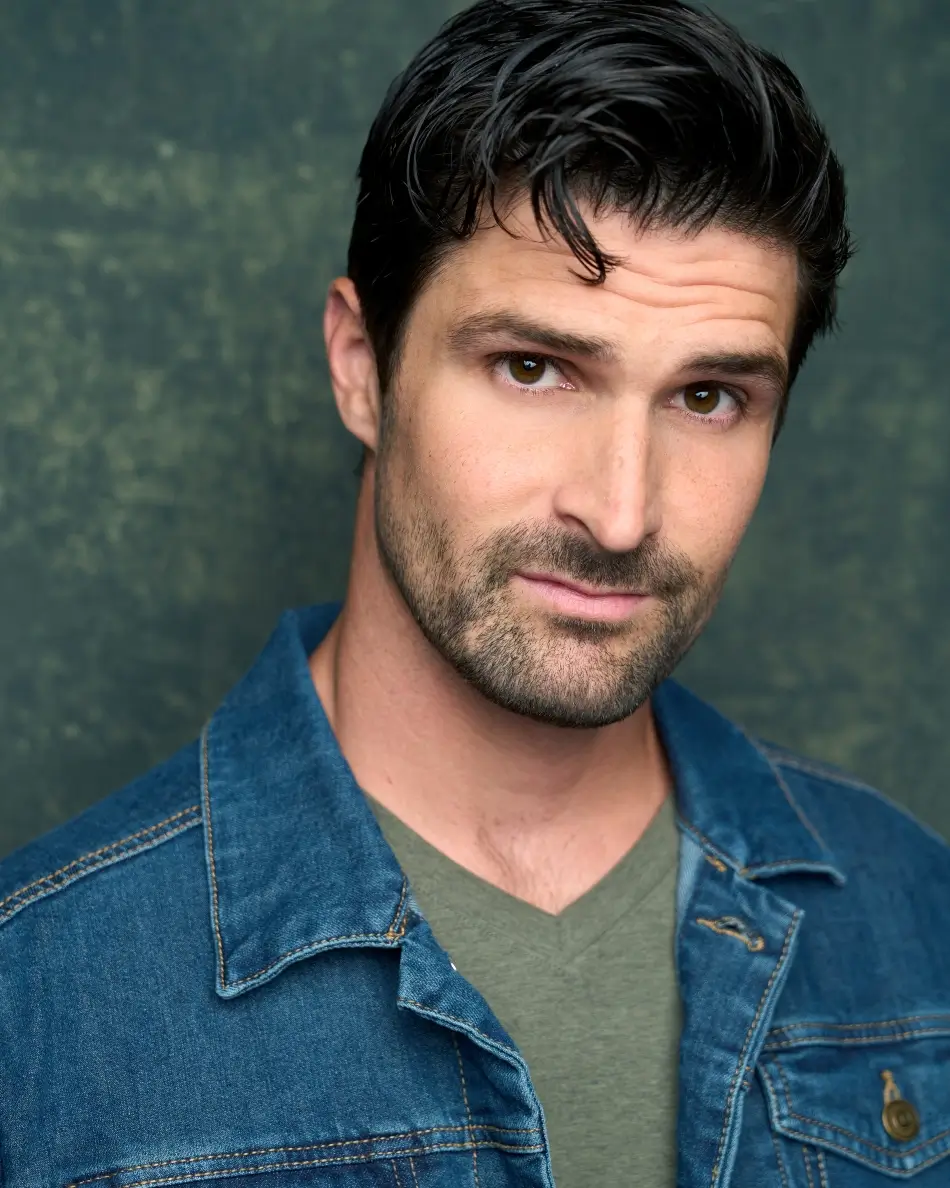 Atlanta men’s actor headshot — young male with dark hair, rugged expression in denim jacket and olive shirt against textured background, theatrical leading man look.