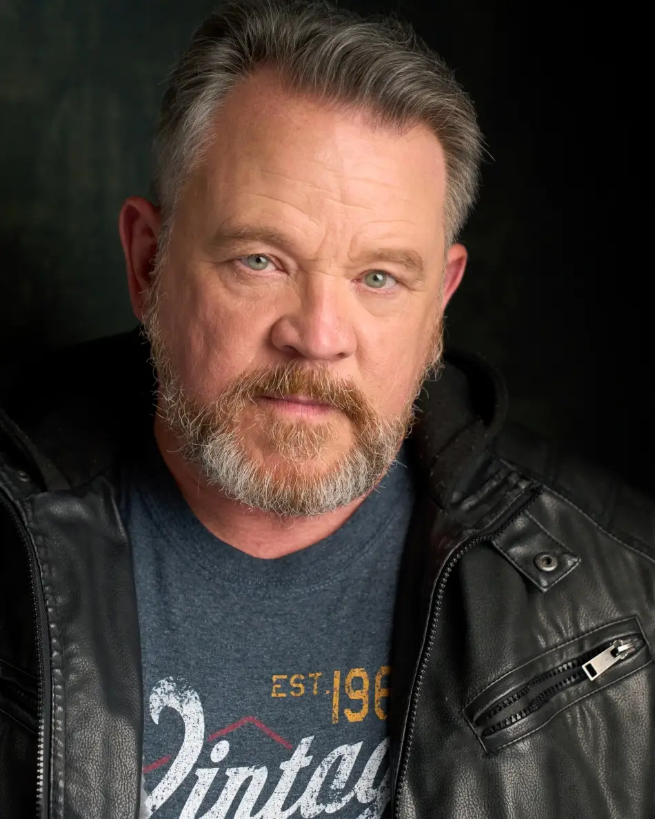 Atlanta men’s actor headshot — mature male with beard and salt-and-pepper hair, intense expression in leather jacket and vintage t-shirt, edgy theatrical look for gritty drama roles.