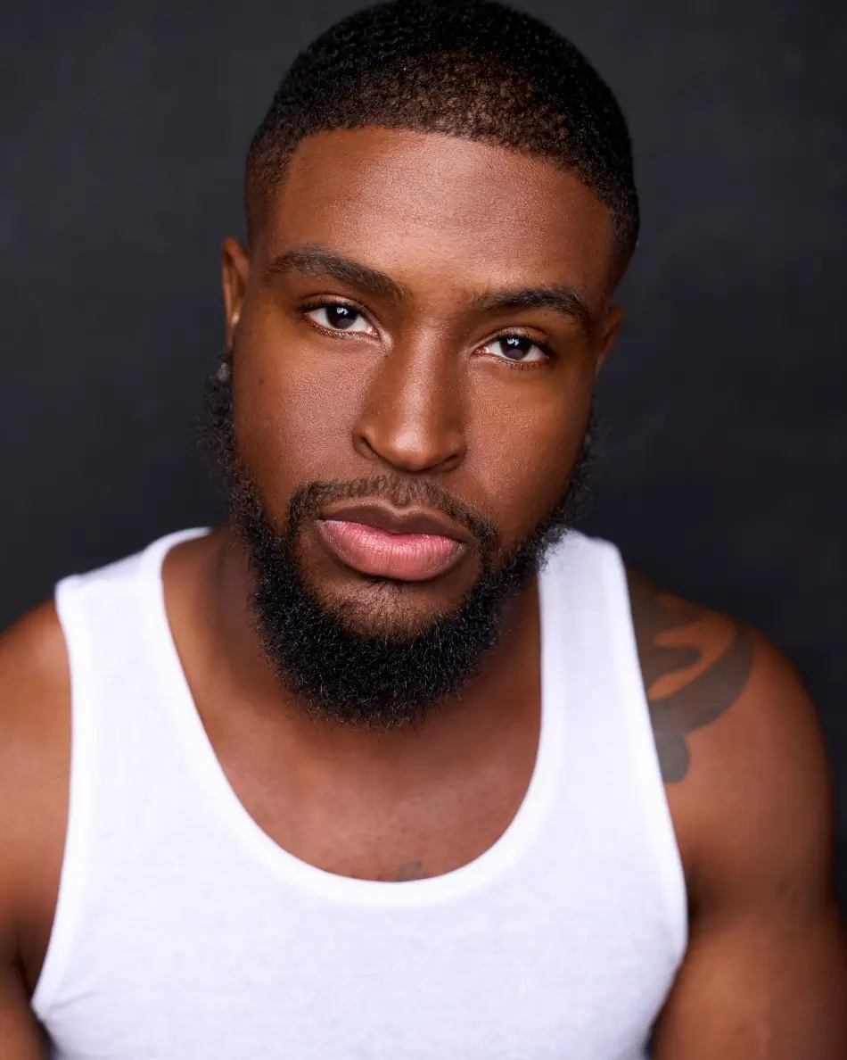 Atlanta men’s actor headshot — male actor in white tank top with confident expression and direct gaze against dark background, strong theatrical look with grounded presence.
