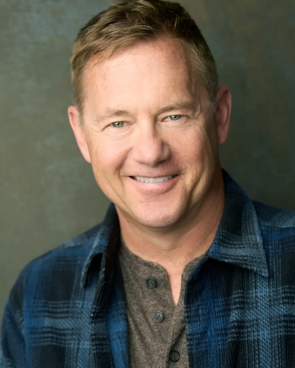Atlanta men’s actor headshot — middle-aged male actor with light hair, warm smile in plaid shirt and henley against neutral background, approachable commercial look.