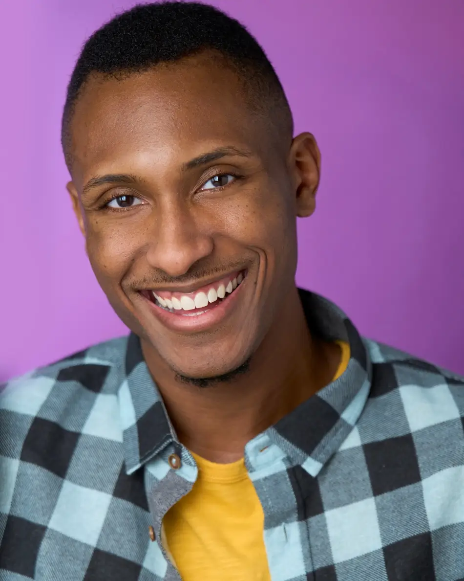 Atlanta men’s actor headshot — young male actor with bright smile in yellow shirt and plaid button-up against purple background, commercial lifestyle and charismatic look.