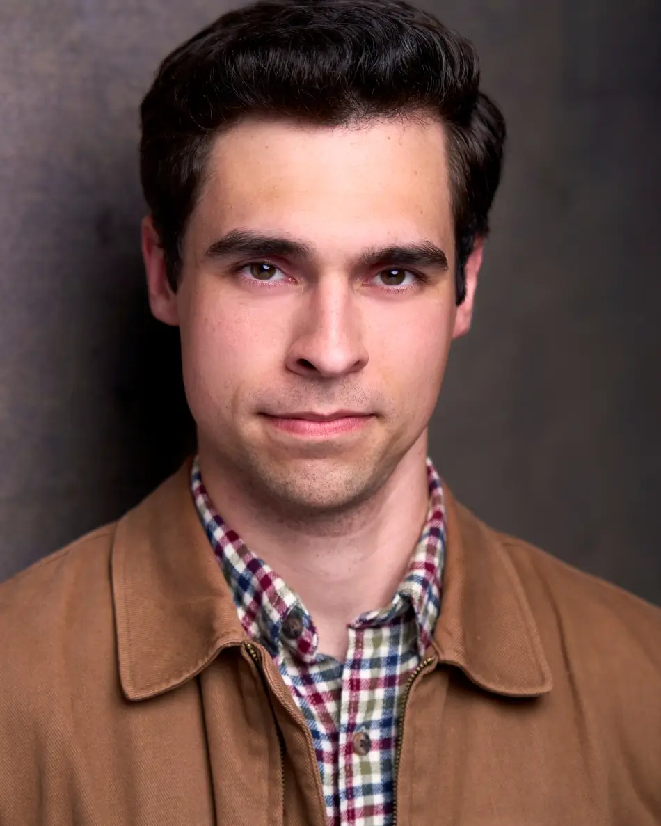 Atlanta men’s actor headshot — young male with dark hair, serious grounded expression in tan jacket and plaid shirt against neutral background, modern theatrical look for dramatic roles.