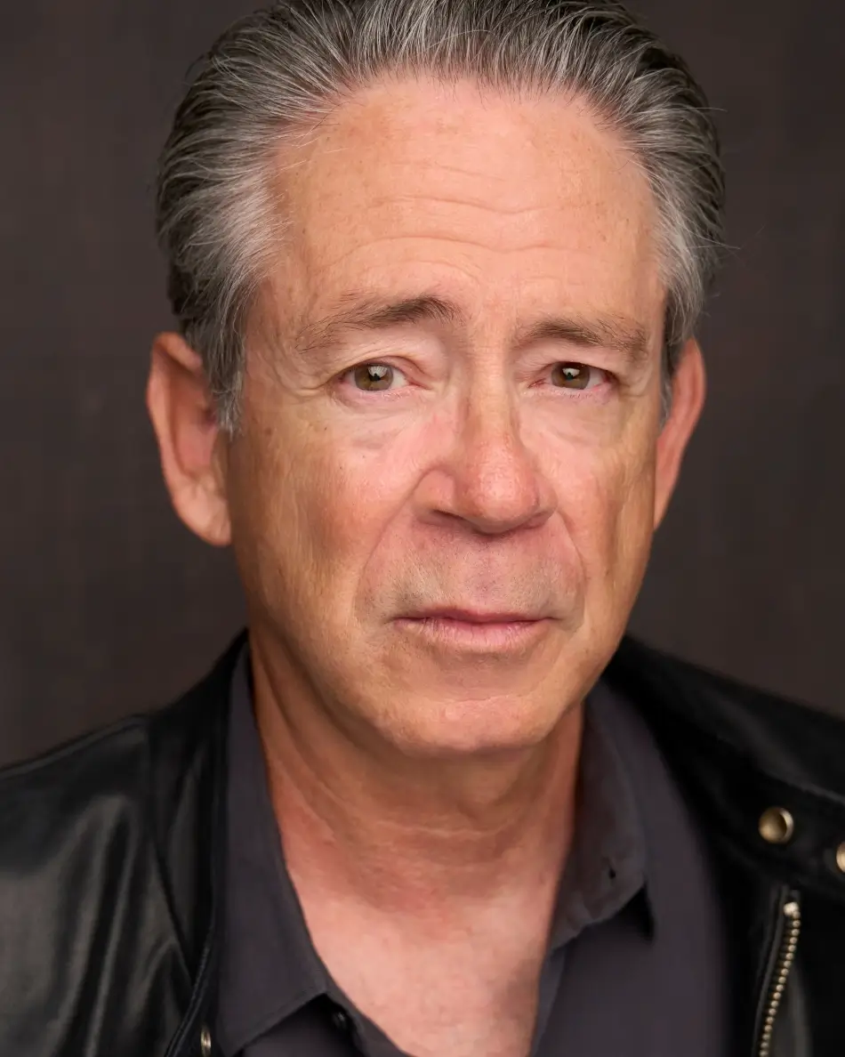 Atlanta men’s actor headshot — mature male with gray hair, serious expression in black shirt and leather jacket against dark background, theatrical gritty mature look.