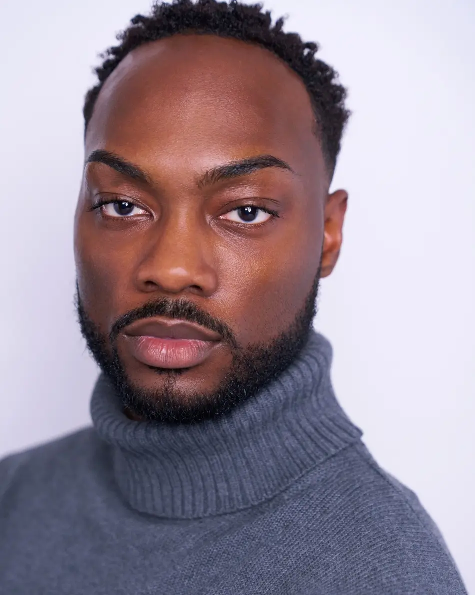 Atlanta men’s actor headshot — mature male with salt-and-pepper hair, subtle confident smile in plaid shirt and graphic tee against neutral background, grounded theatrical character look.