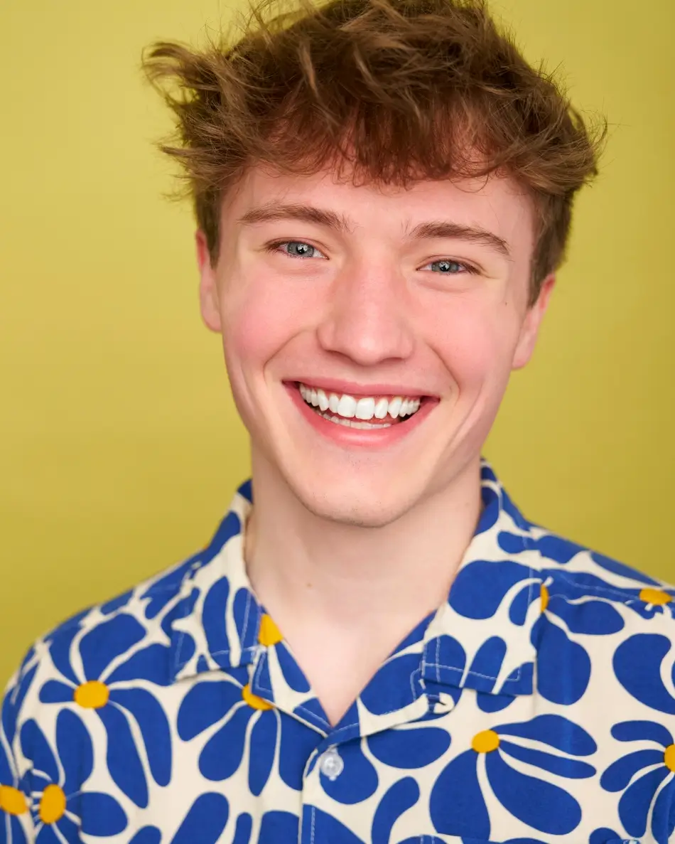Atlanta men’s actor headshot — young male actor with tousled hair and bright smile in bold patterned shirt against yellow background, youthful high-energy commercial look.