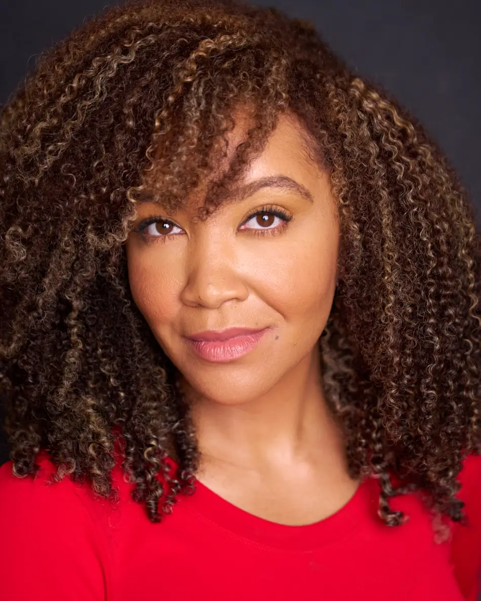 Atlanta theatrical actor headshot — female actor with natural curls, confident closed-mouth smile in a red top, dark studio background.