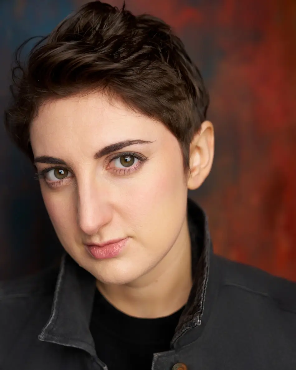 Atlanta theatrical actor headshot — female actor with short dark hair, intense expression in dark jacket against textured red and brown background, edgy dramatic look.