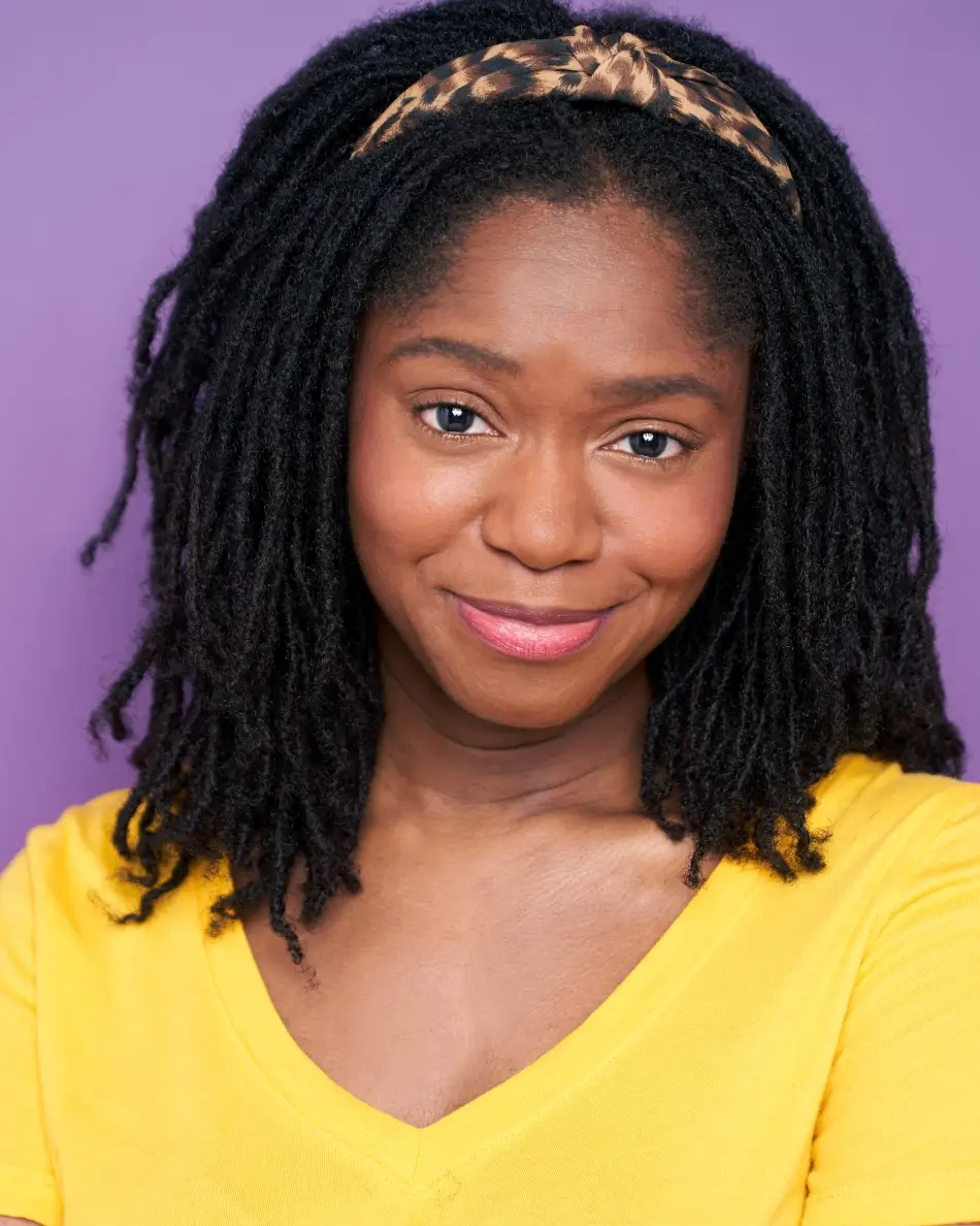 Atlanta commercial actor headshot — female actor with locs, leopard-print headband, warm smile in a yellow top against purple background.