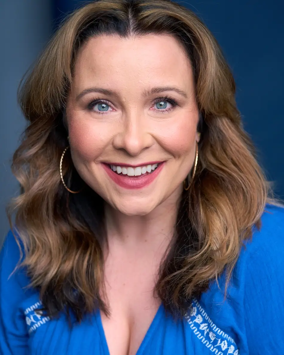 Atlanta commercial actor headshot — female actor with long brown hair, bright toothy smile, hoop earrings, blue top, approachable and friendly expression.