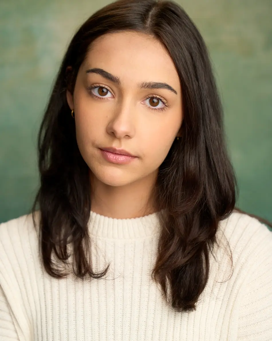 Atlanta theatrical actor headshot — young female with long dark hair in white sweater, serious thoughtful expression against green studio background, ideal for TV drama roles.