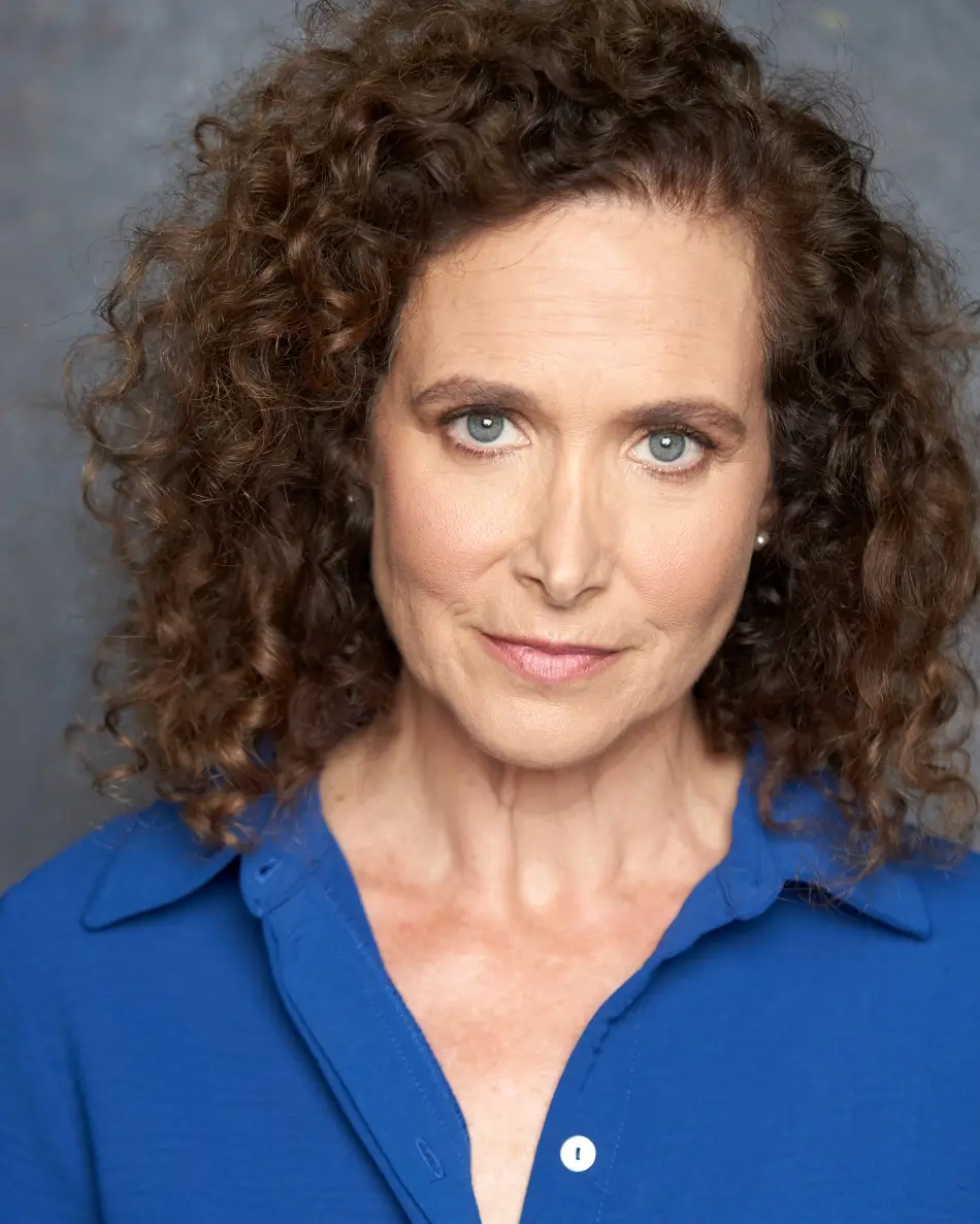 Atlanta theatrical actor headshot — mature female actor with curly hair, serious professional expression in blue blouse, strong authority type.