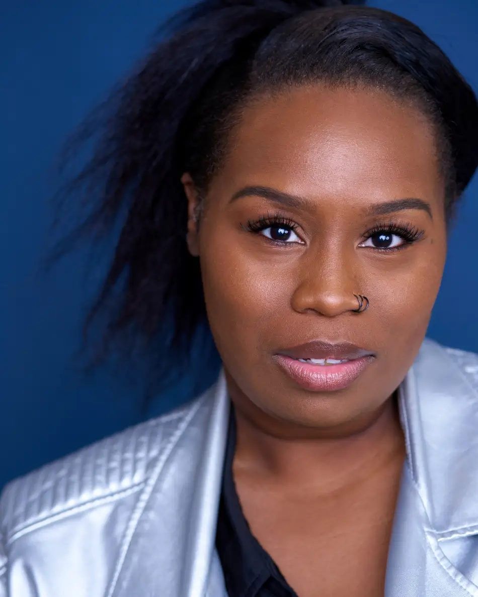 Atlanta theatrical actor headshot — female actor with confident expression, nose ring, silver jacket against dark blue background, dramatic and edgy professional look.