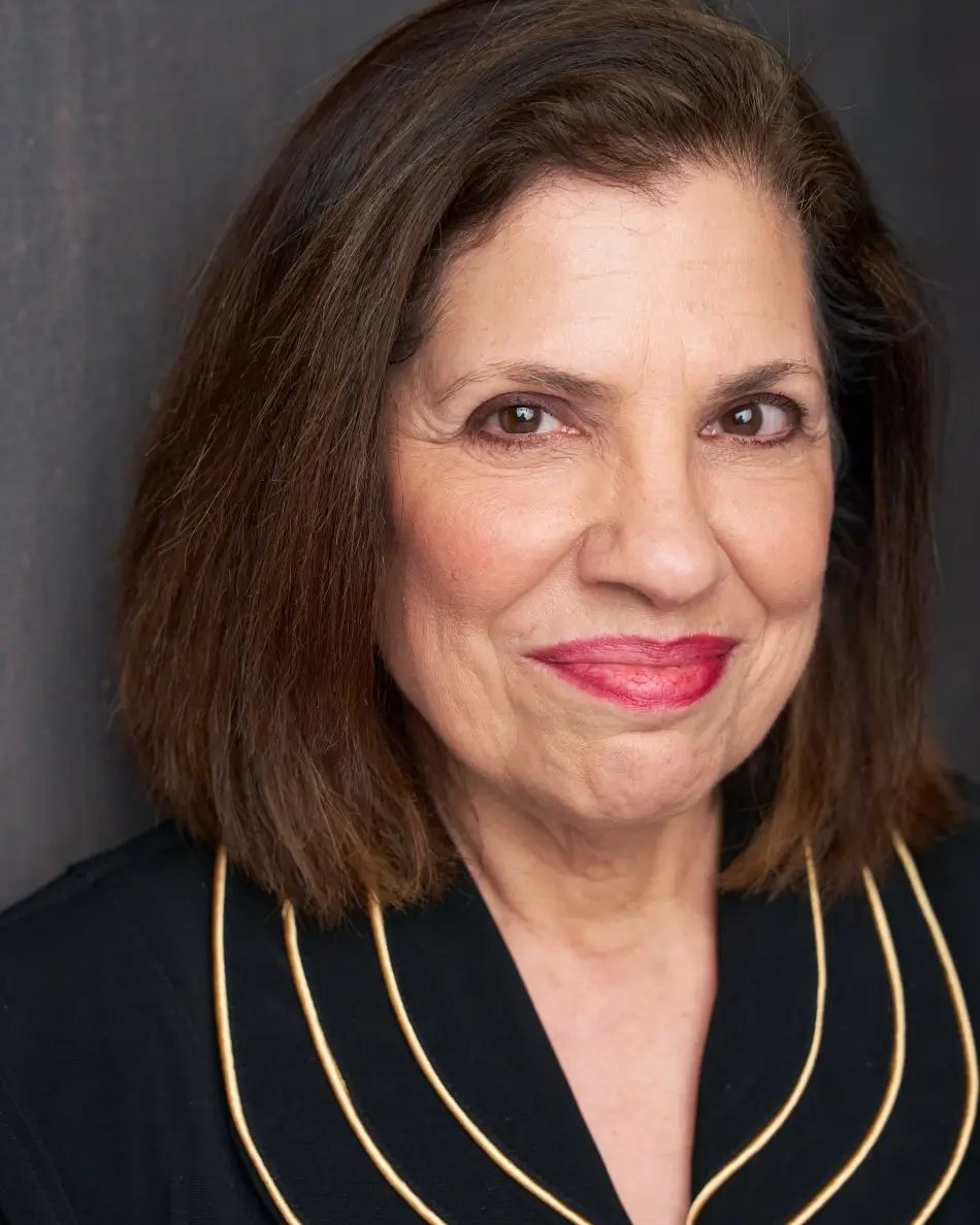 Atlanta theatrical actor headshot — mature female actor with short brown hair, confident smile in black top with gold trim, authority and matriarch role type.