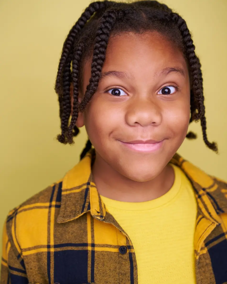 Atlanta kids actor headshot — young boy with braids, bright eyes, and playful expression in yellow plaid shirt and yellow tee against matching background, expressive commercial kids look.