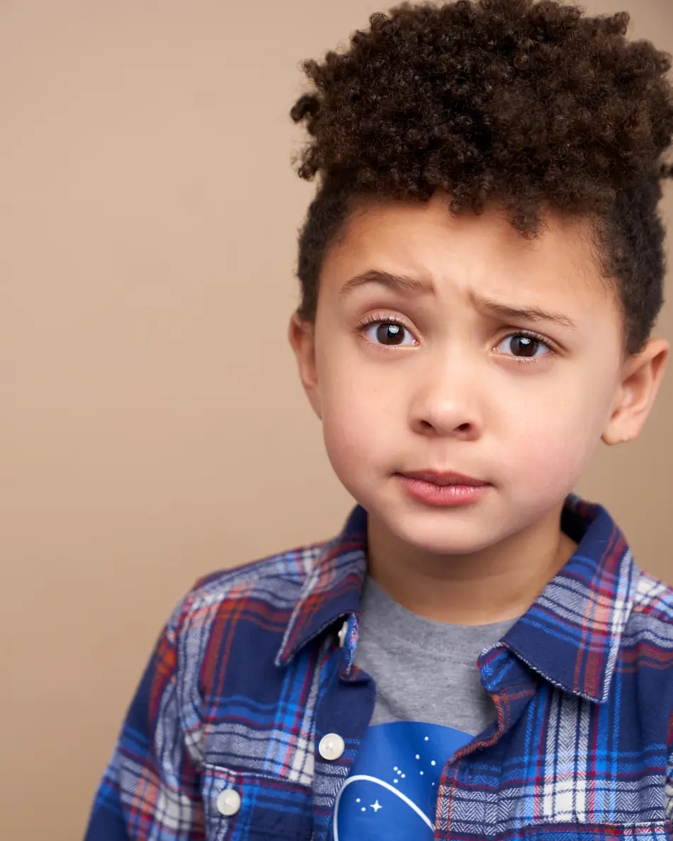 Atlanta kids actor headshot — young boy with curly hair and raised eyebrow expression in plaid shirt against neutral background, expressive theatrical kids character look.