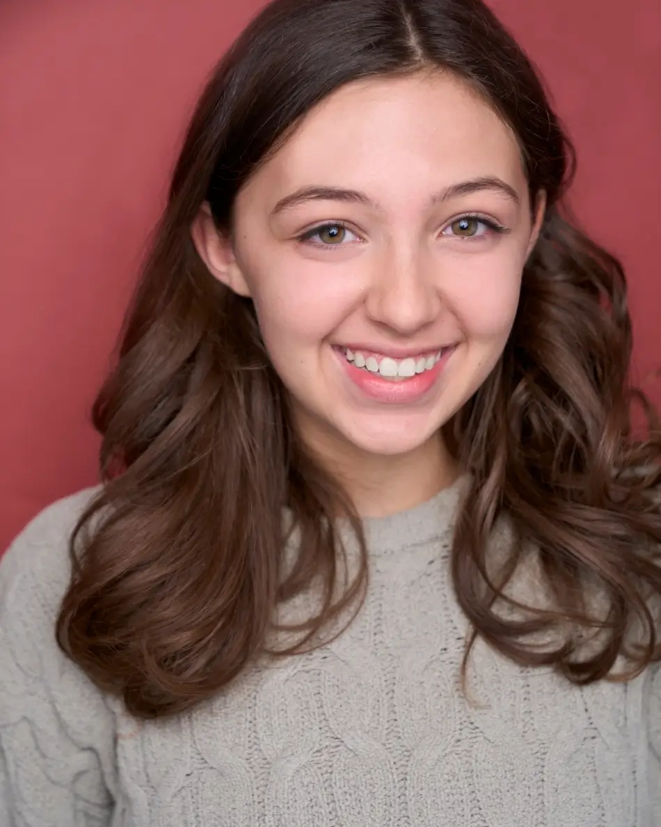 Atlanta teen actor headshot — teen girl with long brown hair, big smile in gray sweater against red background, warm approachable commercial teen look.