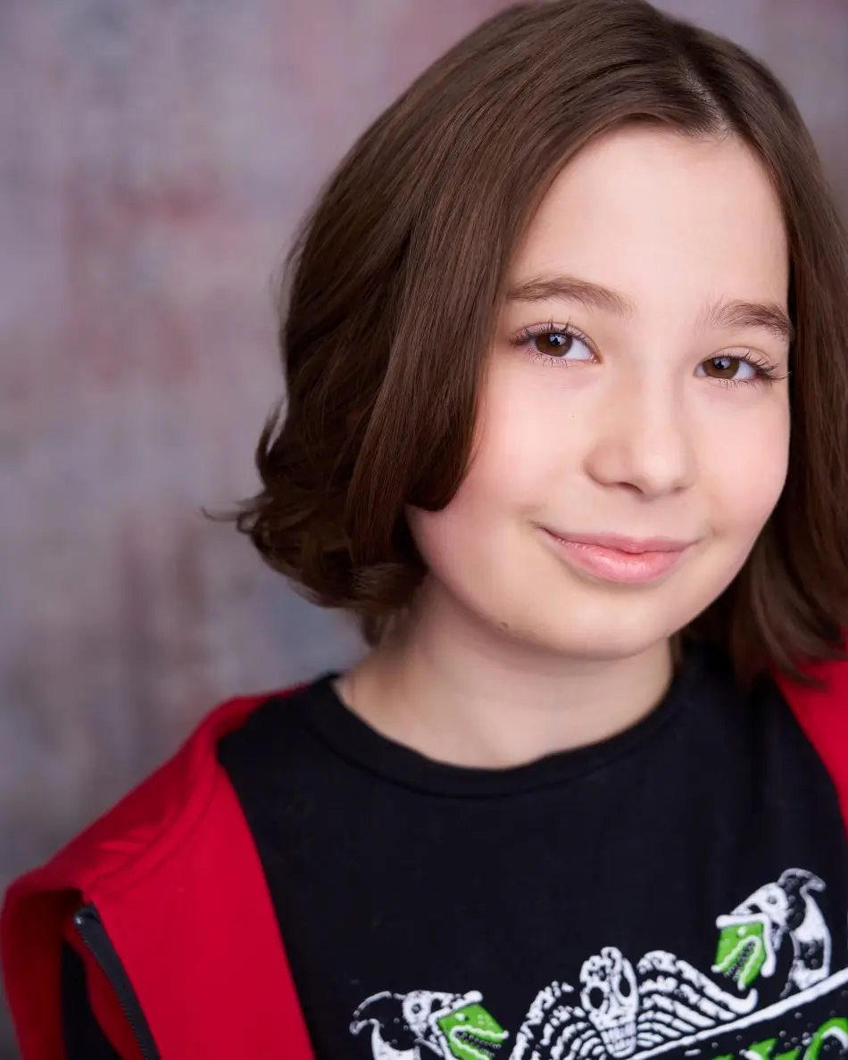 Atlanta kids actor headshot — young child with medium-length brown hair, confident smirk in red hoodie and graphic tee against textured background, theatrical character kids look.