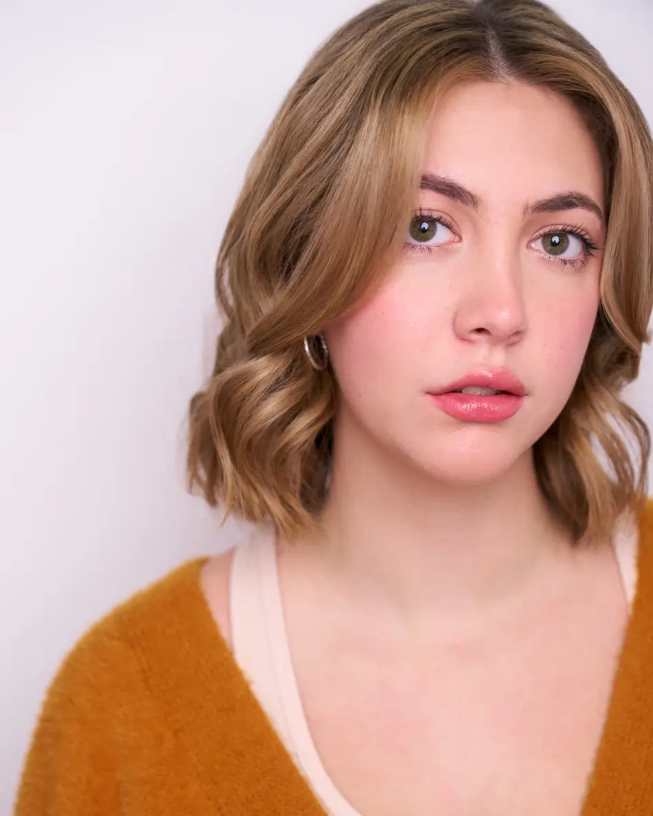 Atlanta teen actor headshot — teen girl with short blonde hair, serious subtle expression in mustard sweater and neutral top against light background, mature theatrical teen look for drama roles.