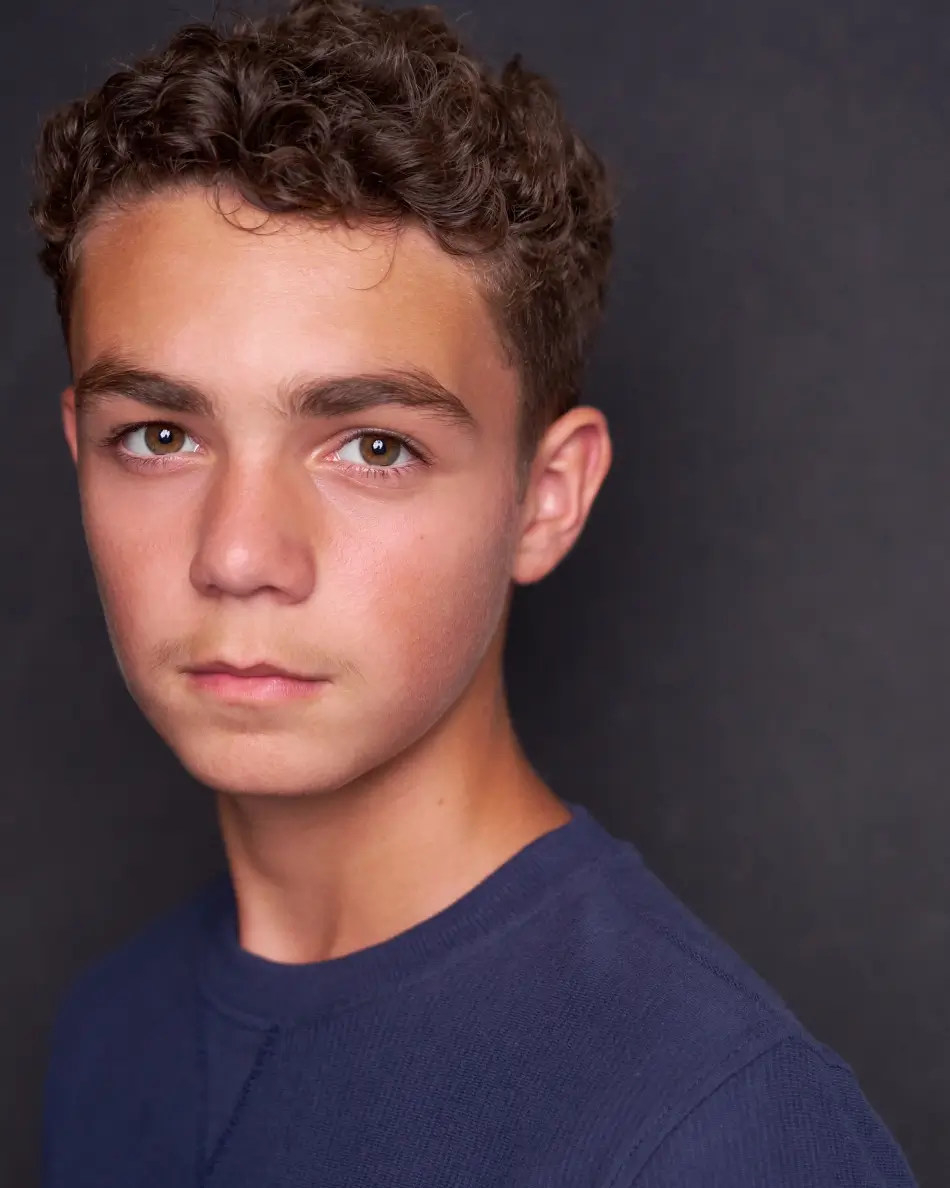 Atlanta teen actor headshot — teenage boy with curly hair, serious grounded expression in navy shirt against dark background, theatrical drama-ready teen look.