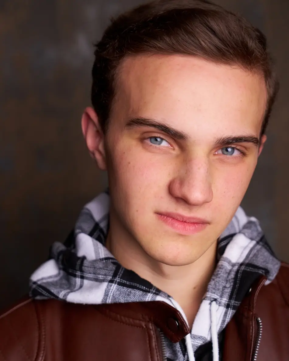 Atlanta teen actor headshot — teenage boy with short brown hair, confident intense expression in plaid hoodie and leather jacket against dark background, edgy theatrical drama teen look.